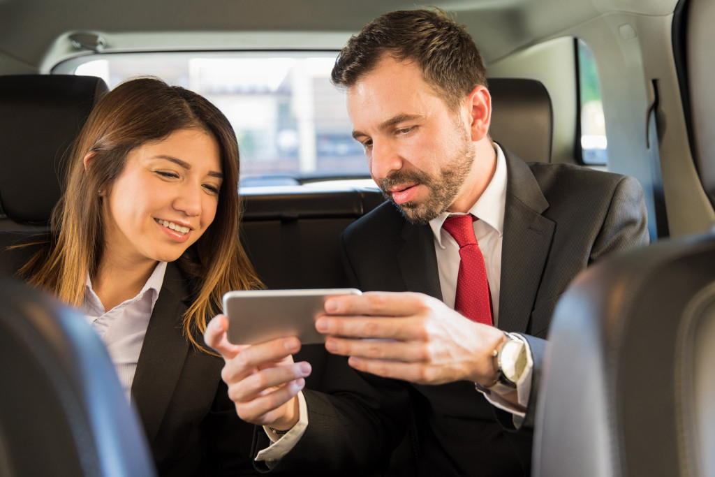 Portrait of two young businesspeople riding in the backseat of a car and looking at a smartphone