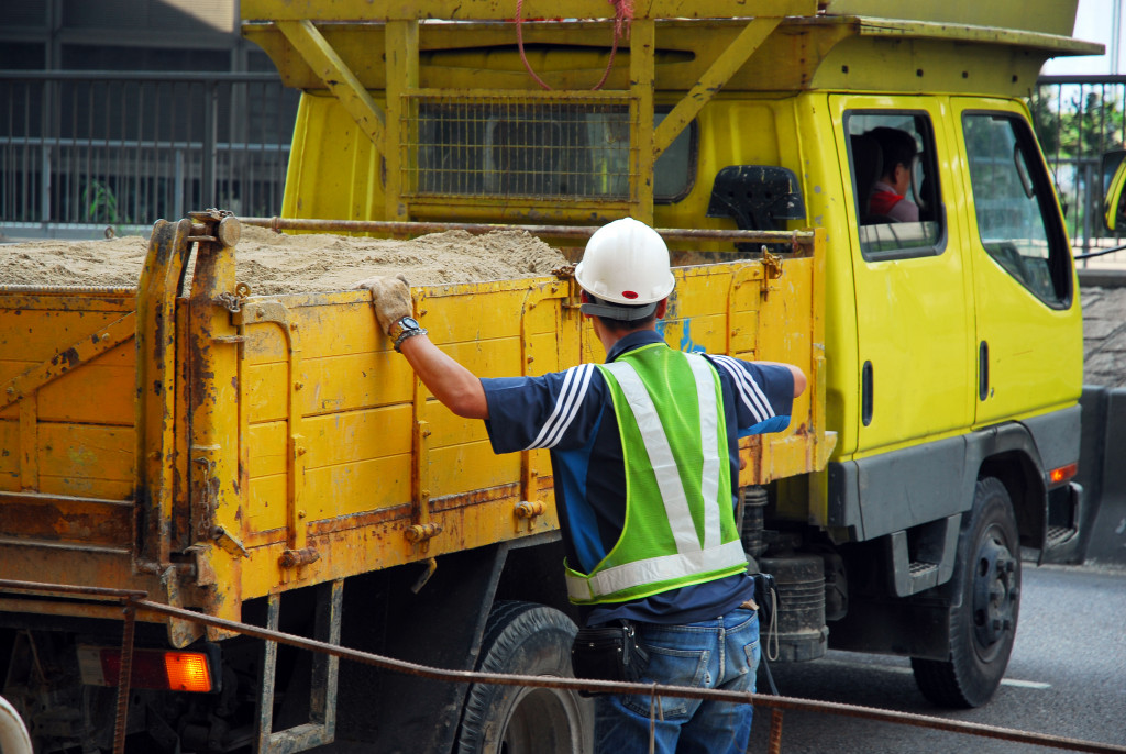 A man in construction gear helping the driver of a dump truck filled with sand park
